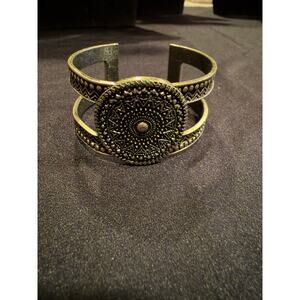 Antiqued brass bracelet with sunburst textures is centered on a double-band cuff